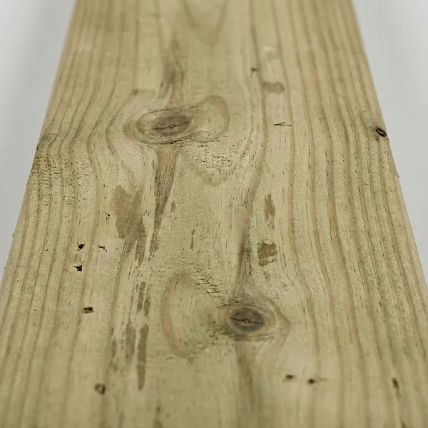Close-up detail of pressure-treated pine lumber showing natural wood grain patterns and knots with a light greenish-tan coloration typical of chemical treatment.